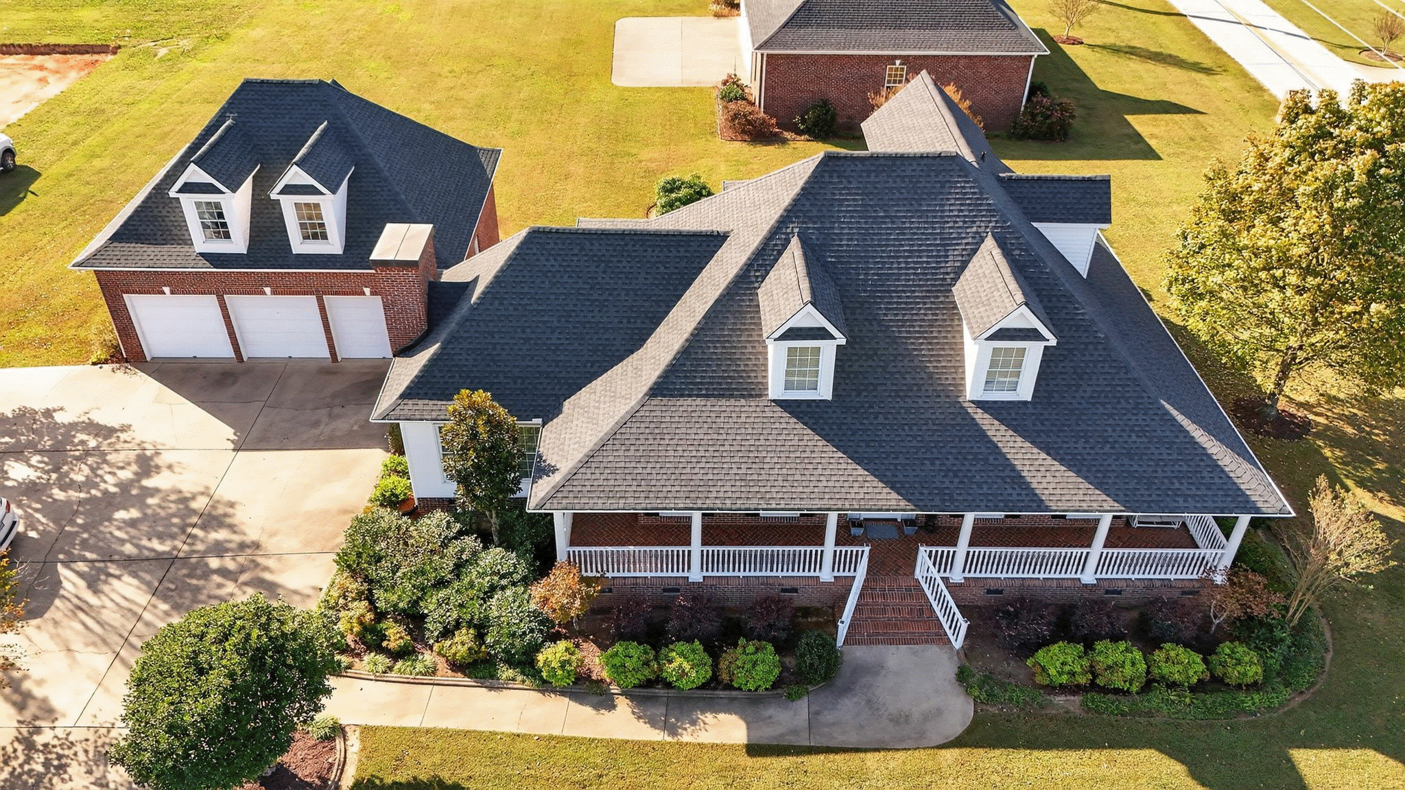 Aerial view of a spacious brick home featuring a large front porch and landscaped yard, highlighting its charming design and modern setting.