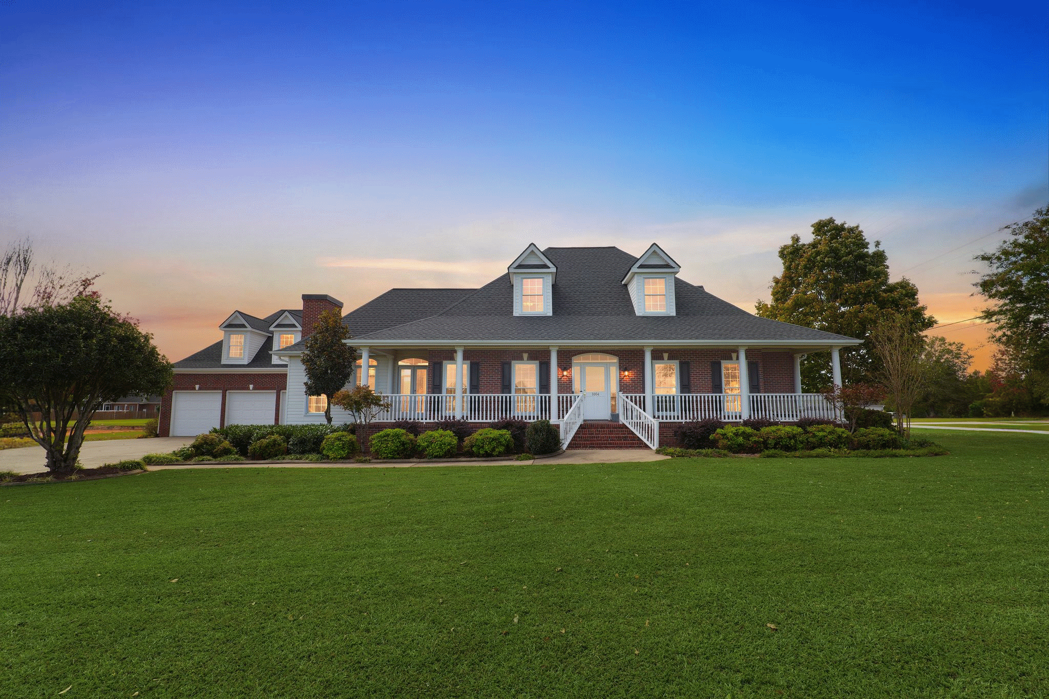 Charming two-story house with a front porch, manicured lawn, and clear evening sky. Ideal for showcasing residential real estate.
